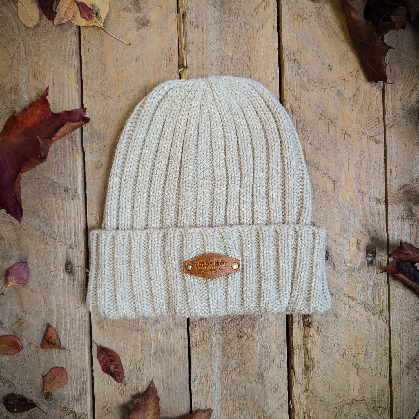 Knitted beanie with a brand logo on a wooden surface with autumn leaves