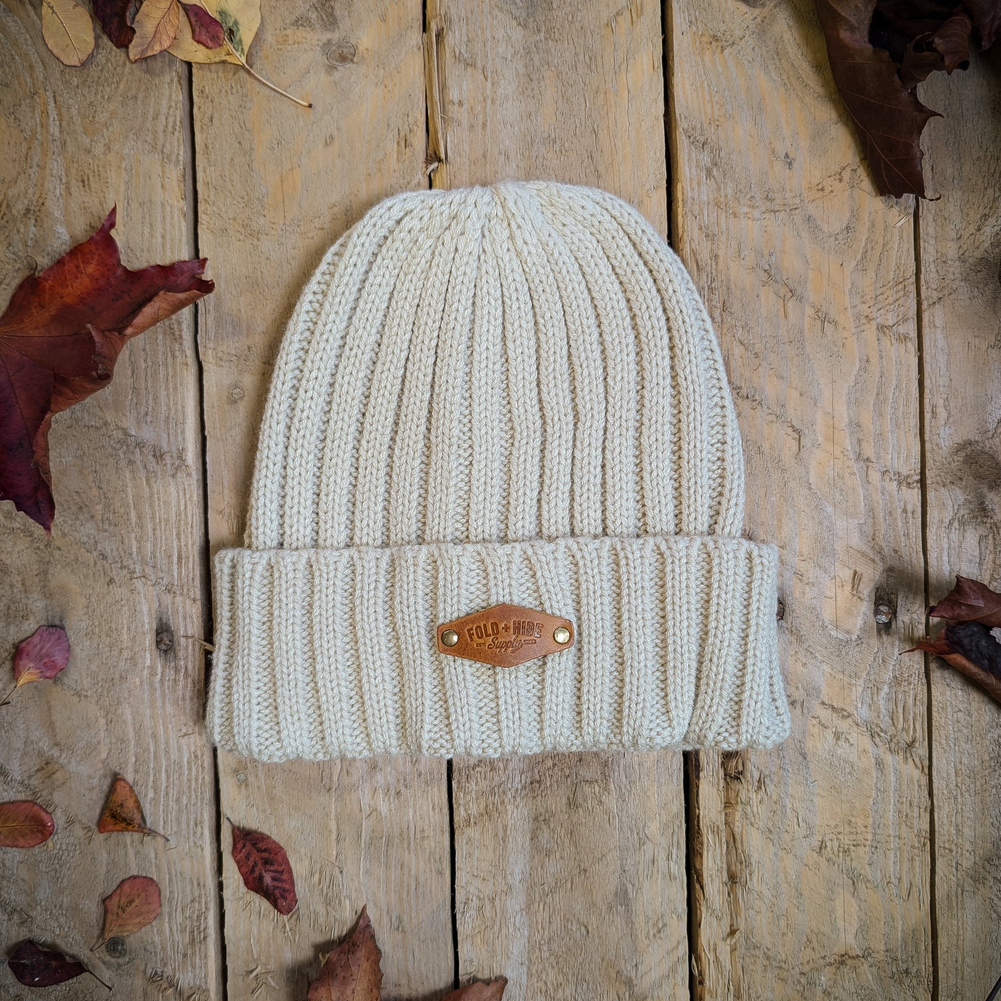 Knitted beanie with a brand logo on a wooden surface with autumn leaves